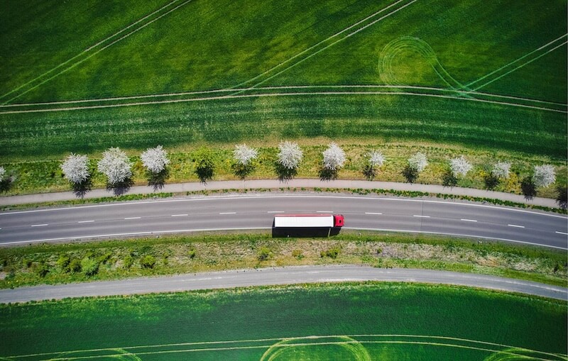 Ein roter LKW mit weißem Dach fährt durch eine Frühlingslandschaft mit satten Grüntönen