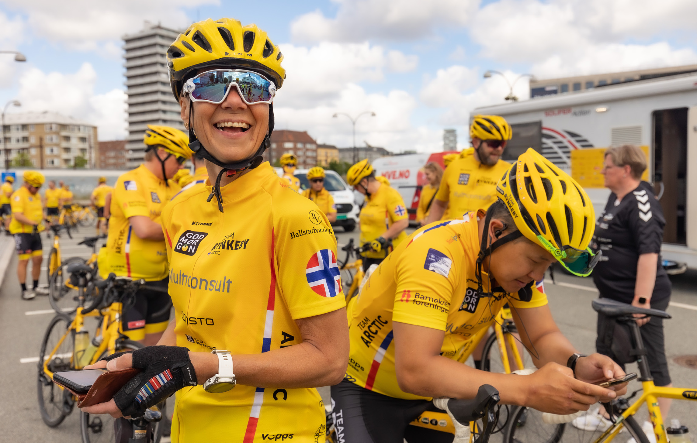 Fahrradfahrer stehen in einer Gruppe zusammen. Sie tragen gelbe Trikots und Helme und die norwegische Flagge auf dem linken Ärmel