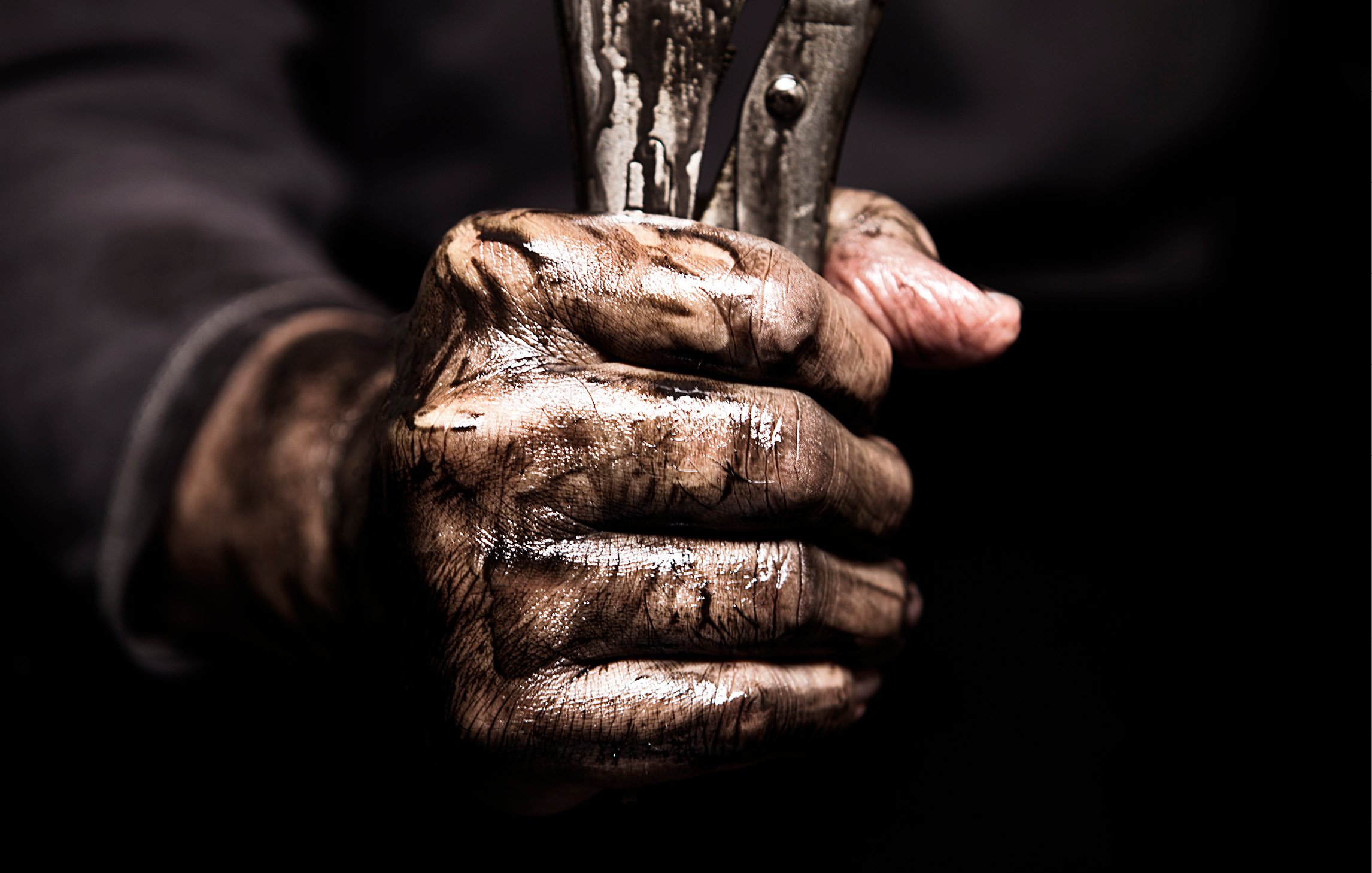 Nahaufnahme einer ölverschmierten Hand, die ein metallenes Werkzeug hält.