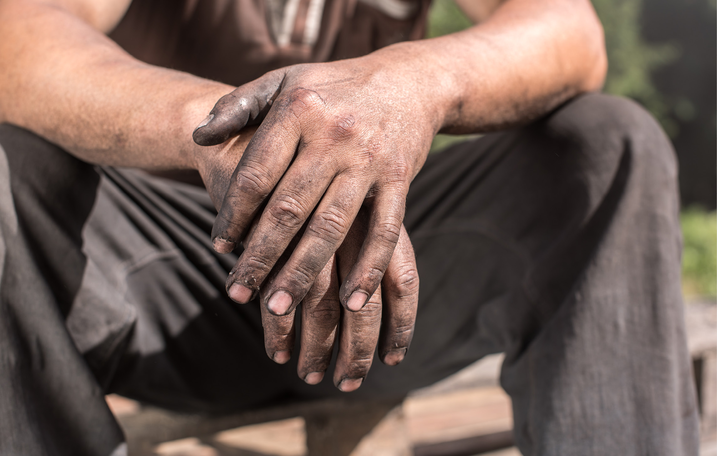 Ein Mann sitzt in Arbeitskleidung und mit schmutzigen Händen auf einer Kante 
