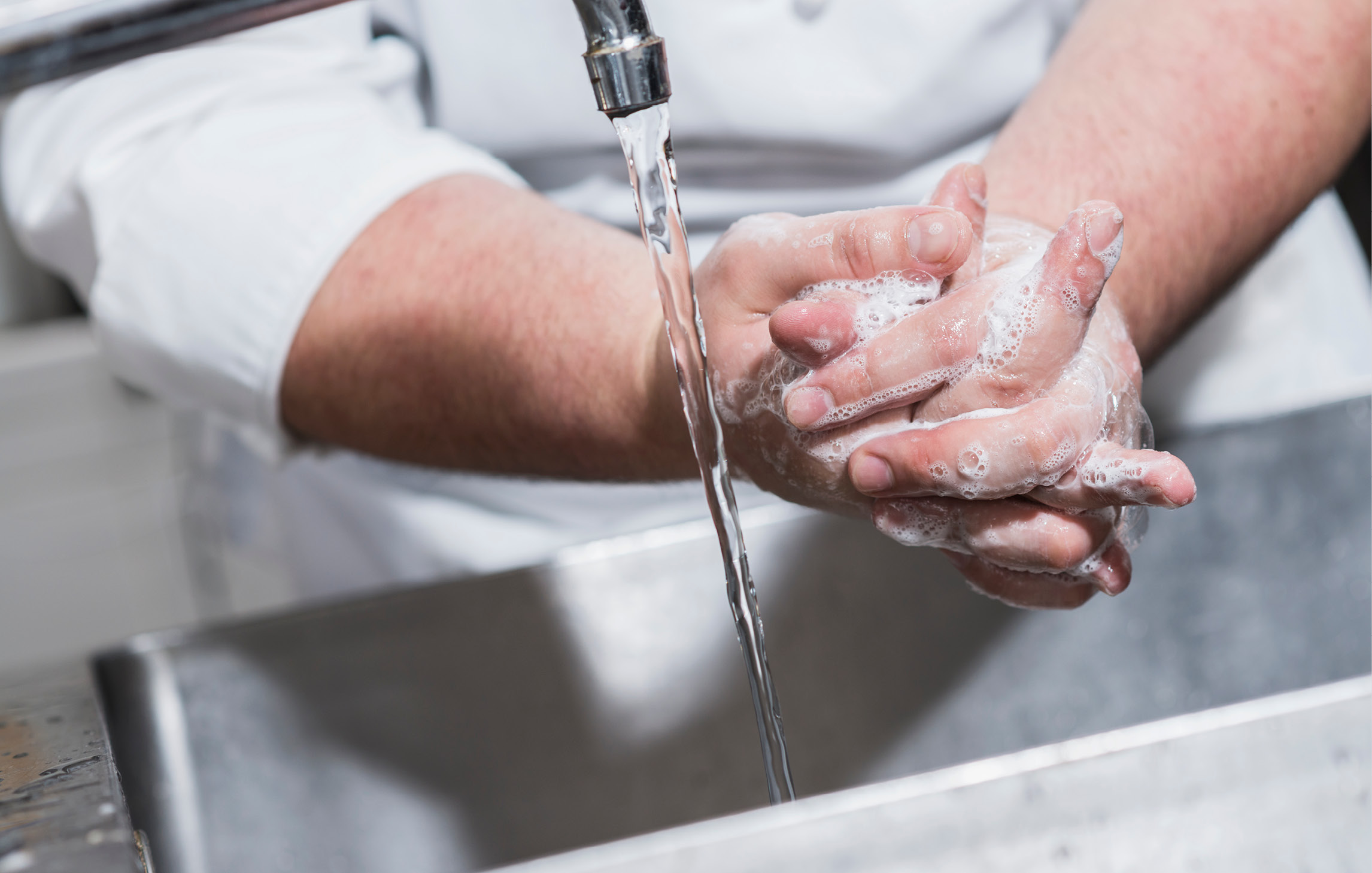 Ein Mann in weißer Kleidung reinigt sich an einem Waschbecken die Hände