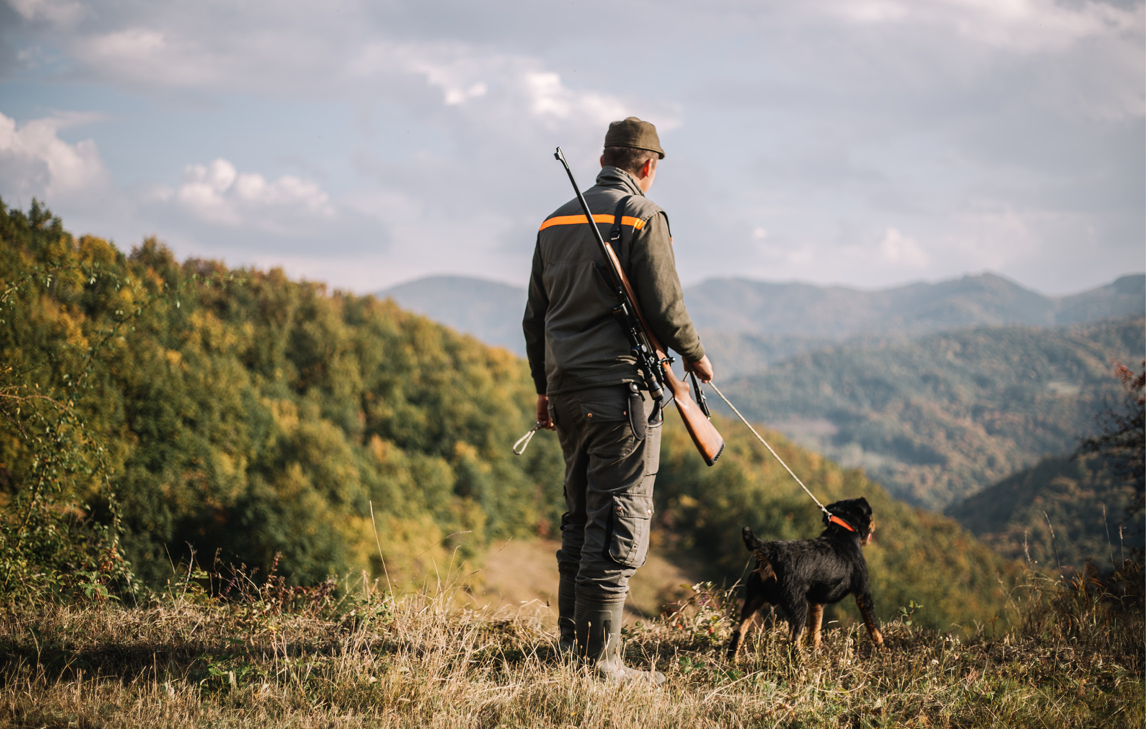 Ein Jäger steht mit seinem Jagdhund in der Natur und schaut in die Ferne